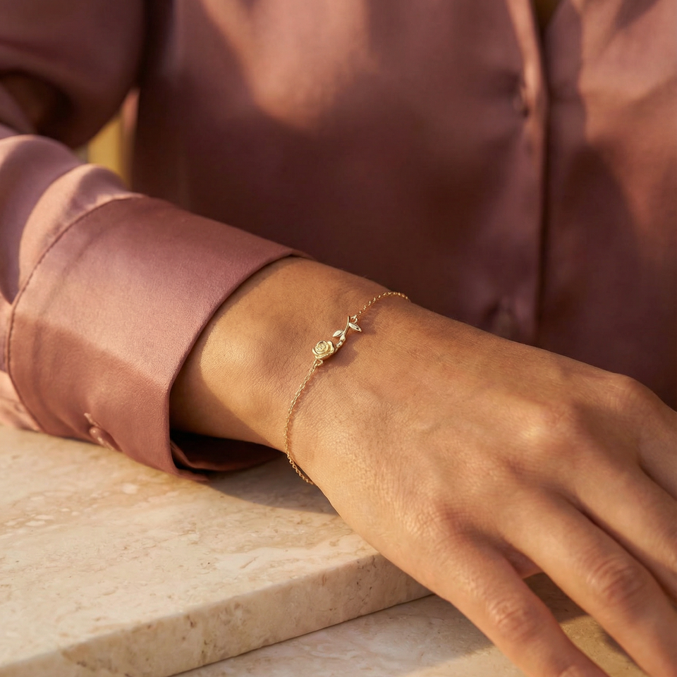 Close-up of a hand wearing a delicate gold rose bracelet on a neutral background